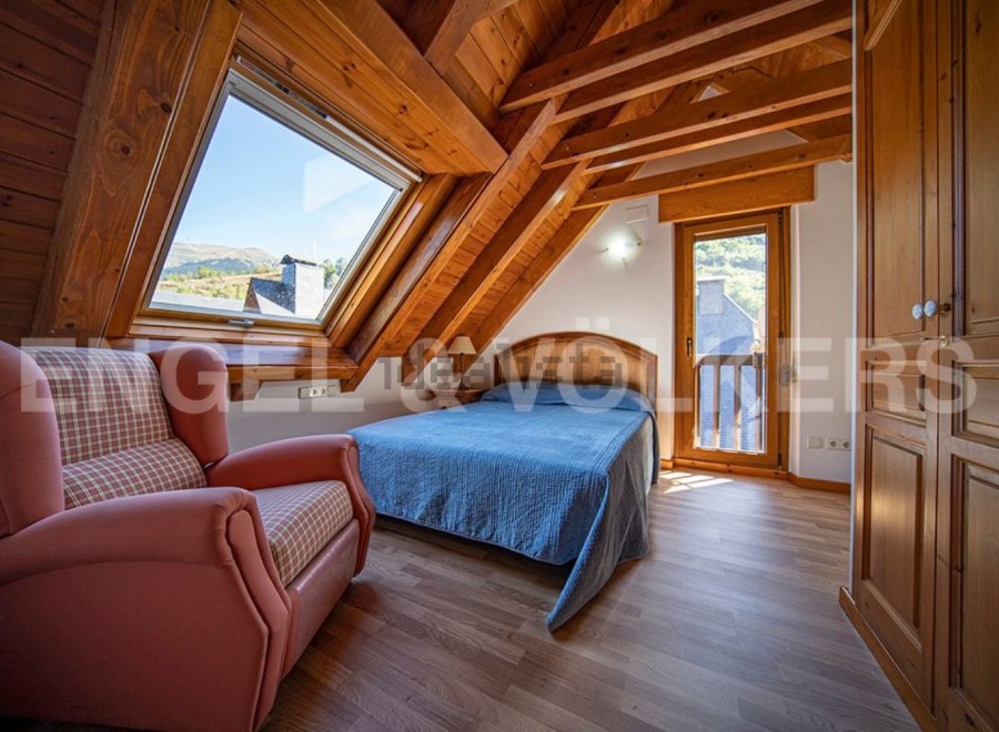 Cozy attic bedroom with wooden beams, large window offering mountain views, and built-in wardrobe.