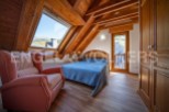 Cozy attic bedroom with wooden beams, large window offering mountain views, and built-in wardrobe.