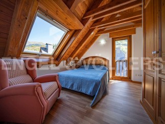 Cozy attic bedroom with wooden beams, large window offering mountain views, and built-in wardrobe.