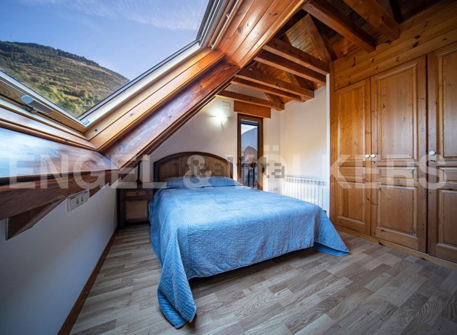 Cozy attic bedroom with wooden beams and skylights offering stunning mountain views.
