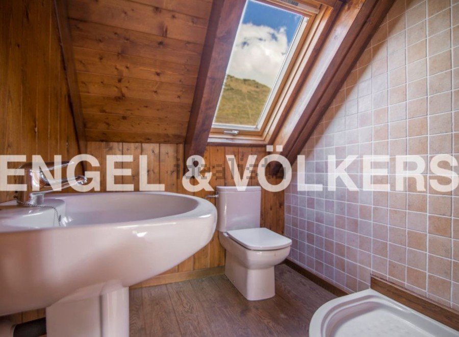 Charming attic bathroom with wooden beams, skylight, and tiled walls.