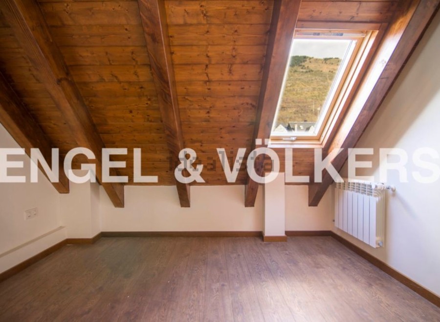 Charming attic room with wooden beams and skylight offering scenic views.
