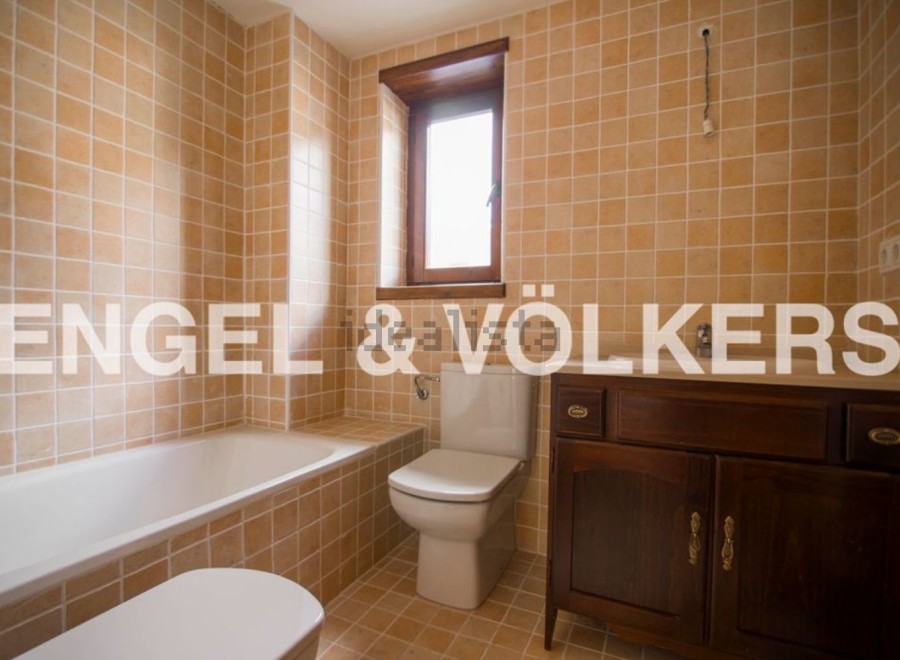 This charming bathroom boasts a classic design with light beige tiles, a built-in bathtub, and a wooden vanity.