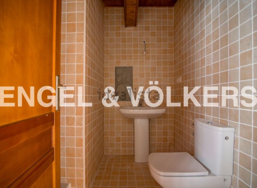 This charming bathroom boasts a modern toilet and pedestal sink, complemented by warm, earthy-toned tiles.