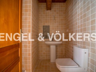 This charming bathroom boasts a modern toilet and pedestal sink, complemented by warm, earthy-toned tiles.