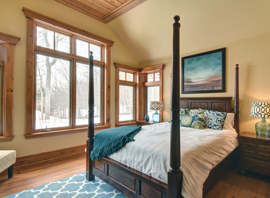 This cozy bedroom features a beautiful four-poster bed and a stunning view of the winter landscape through large windows.