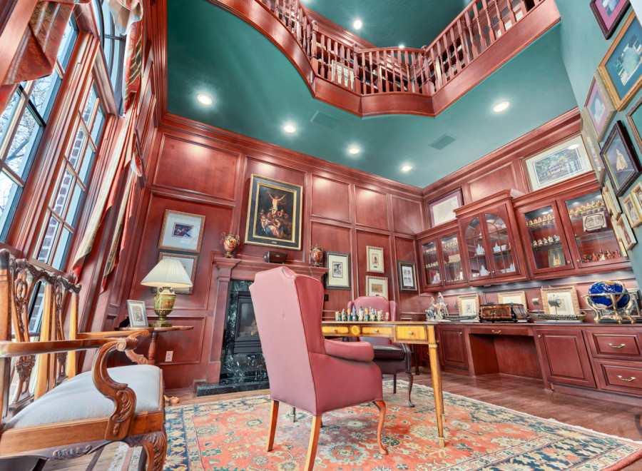 Step into luxury with this stunning home office, featuring rich wood paneling and a grand staircase.