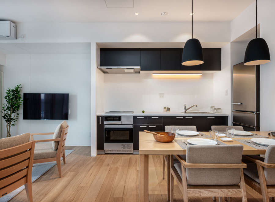 Modern apartment boasts an open-plan kitchen and living area, featuring sleek black cabinetry, integrated appliances, and a light wood dining table.