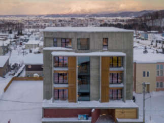 This stunning concrete building boasts a modern design with large windows and wooden accents, offering breathtaking views of the snow-covered landscape and distant mountains.