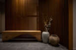 This modern and minimalist hallway features a stunning wooden slat wall, a rustic wooden bench, and two unique ceramic pots with delicate branches.