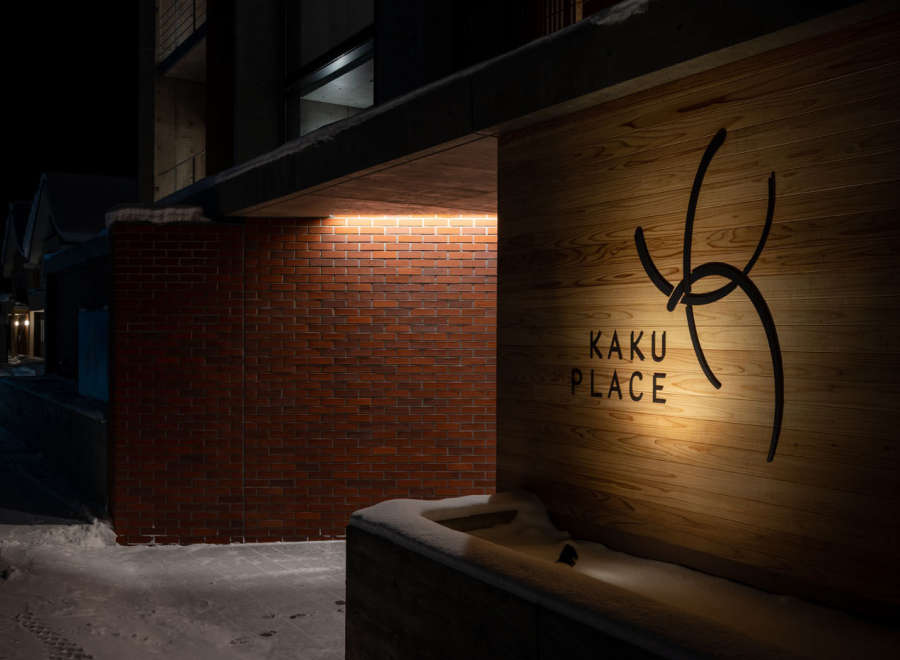 Kaku Place boasts a modern design with a striking brick and wood exterior, illuminated at night for a warm and inviting ambiance.