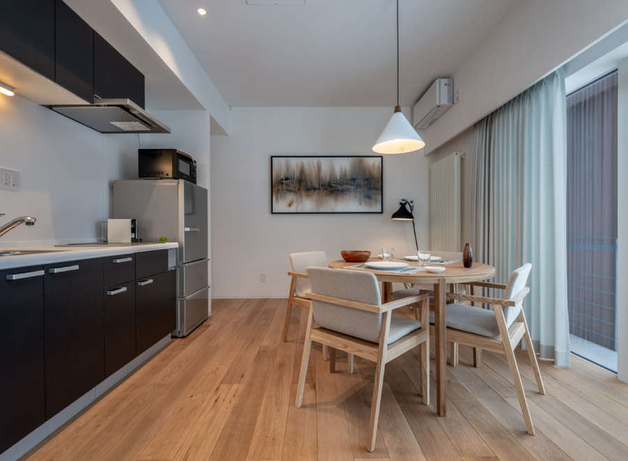 This modern apartment boasts an open-plan kitchen with sleek dark cabinetry and integrated appliances, seamlessly flowing into a dining area with a light wood table and comfortable seating.