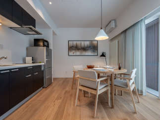 This modern apartment boasts an open-plan kitchen with sleek dark cabinetry and integrated appliances, seamlessly flowing into a dining area with a light wood table and comfortable seating.