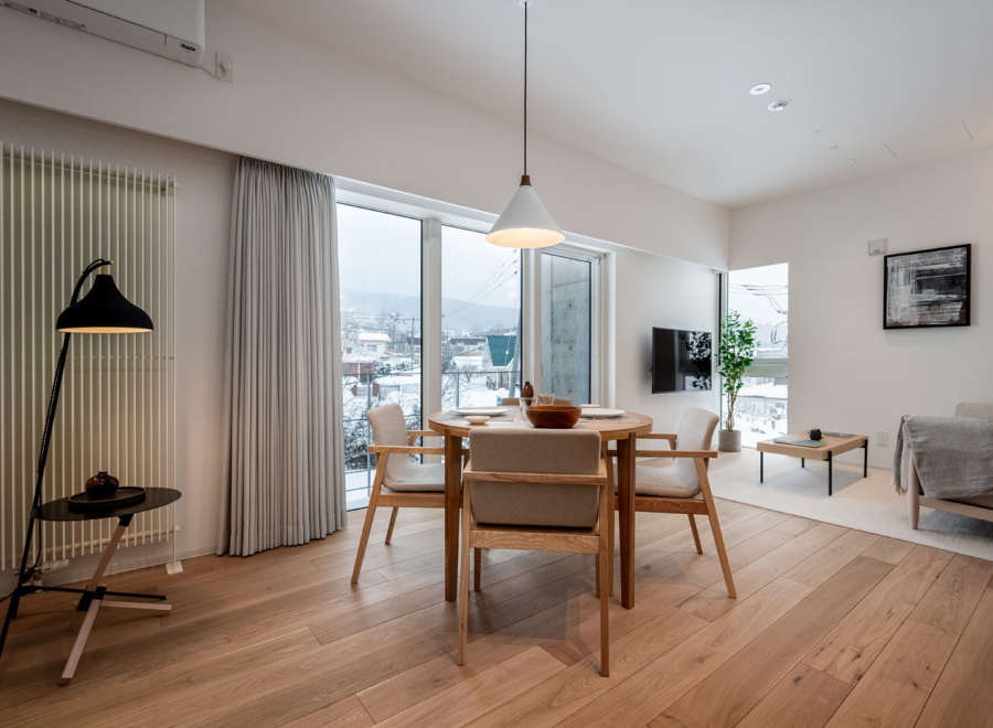 This modern apartment boasts an open-plan living area with hardwood floors, large windows offering scenic views, and a stylish dining set.