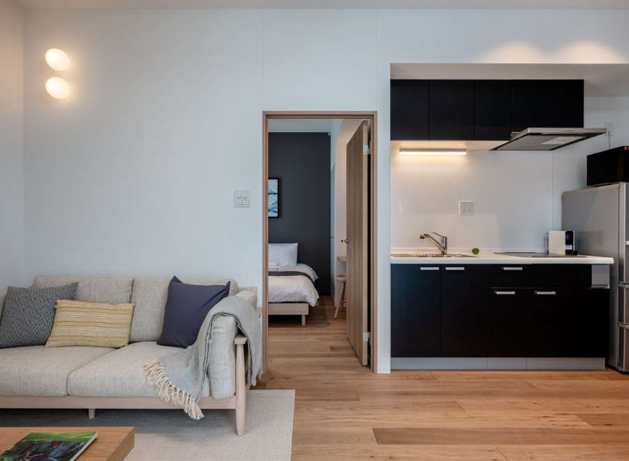 This modern apartment boasts an open-plan living area with a comfortable sofa and a fully equipped kitchen featuring sleek black cabinetry.