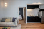This modern apartment boasts an open-plan living area with a comfortable sofa and a fully equipped kitchen featuring sleek black cabinetry.