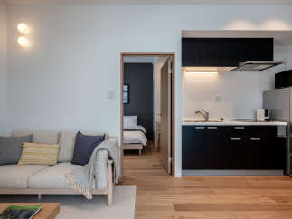 This modern apartment boasts an open-plan living area with a comfortable sofa and a fully equipped kitchen featuring sleek black cabinetry.