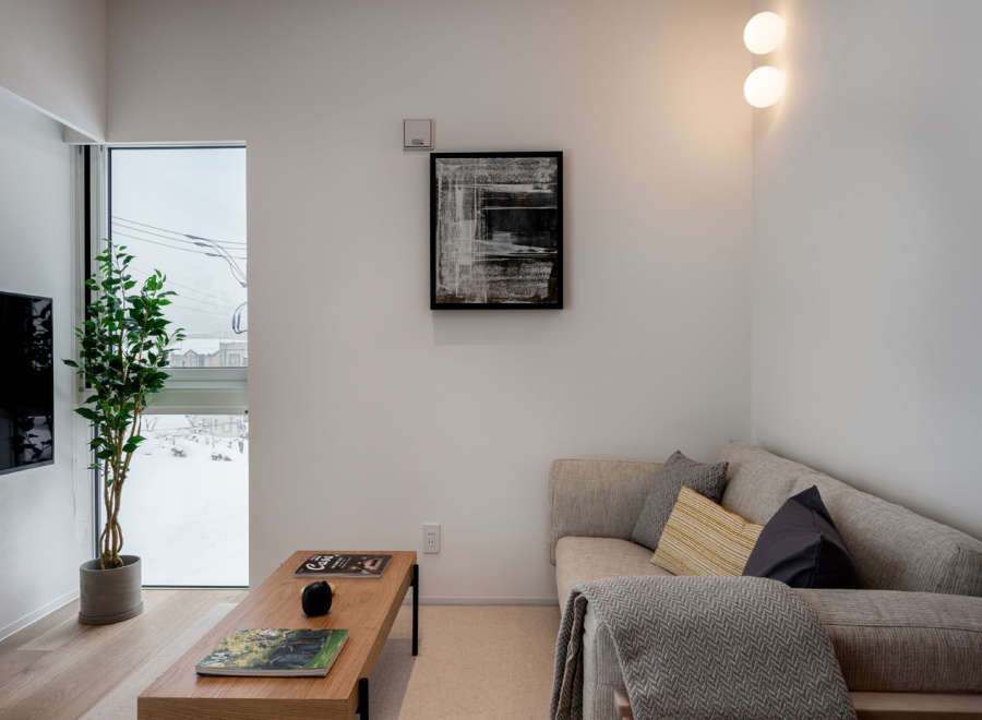 Modern living room with large window offering snowy views, featuring a comfortable corner sofa, stylish coffee table, and tasteful artwork.