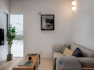 Modern living room with large window offering snowy views, featuring a comfortable corner sofa, stylish coffee table, and tasteful artwork.