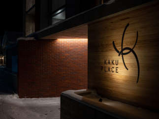 Kaku Place boasts a modern design with a striking brick and wood exterior, illuminated at night for a warm and inviting ambiance.