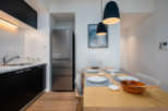 Modern kitchen and dining area with stainless steel refrigerator, sleek black cabinetry, and a light wood dining table.