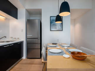 Modern kitchen and dining area with stainless steel refrigerator, sleek black cabinetry, and a light wood dining table.