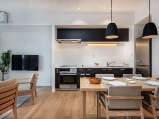 Modern apartment boasts an open-plan kitchen and living area, featuring sleek black cabinetry, integrated appliances, and a light wood dining table.