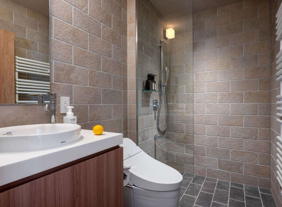 This modern bathroom boasts a sleek design with beige brick walls and dark gray floor tiles.