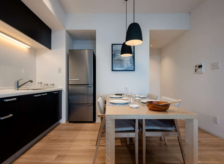 Modern kitchen and dining area with stainless steel refrigerator, sleek black cabinetry, and light wood flooring.