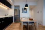 Modern kitchen and dining area with stainless steel refrigerator, sleek black cabinetry, and light wood flooring.