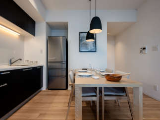Modern kitchen and dining area with stainless steel refrigerator, sleek black cabinetry, and light wood flooring.