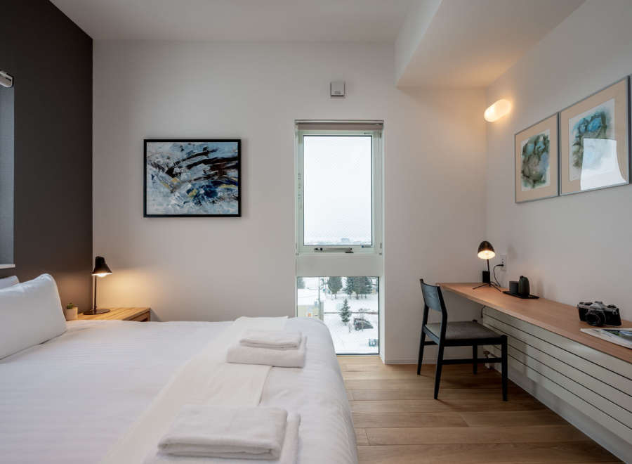This modern bedroom boasts a comfortable queen-size bed with crisp white linens, complemented by a minimalist workspace featuring a sleek desk and chair.