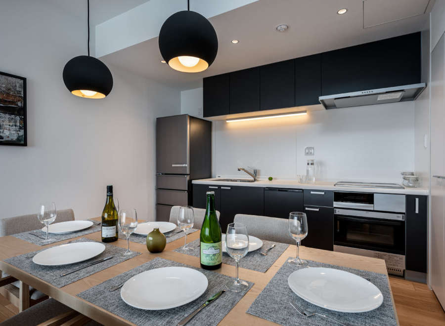 Modern kitchen and dining area with sleek black cabinetry, stainless steel appliances, and stylish pendant lighting.
