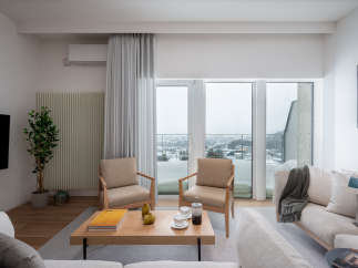 Modern living room with floor-to-ceiling windows offering stunning city views, featuring light beige sofas and armchairs, a wooden coffee table, and a minimalist design aesthetic.