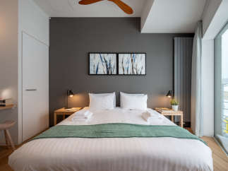 This modern bedroom boasts a king-size bed with crisp white linens and a plush green throw, complemented by minimalist nightstands and stylish artwork.