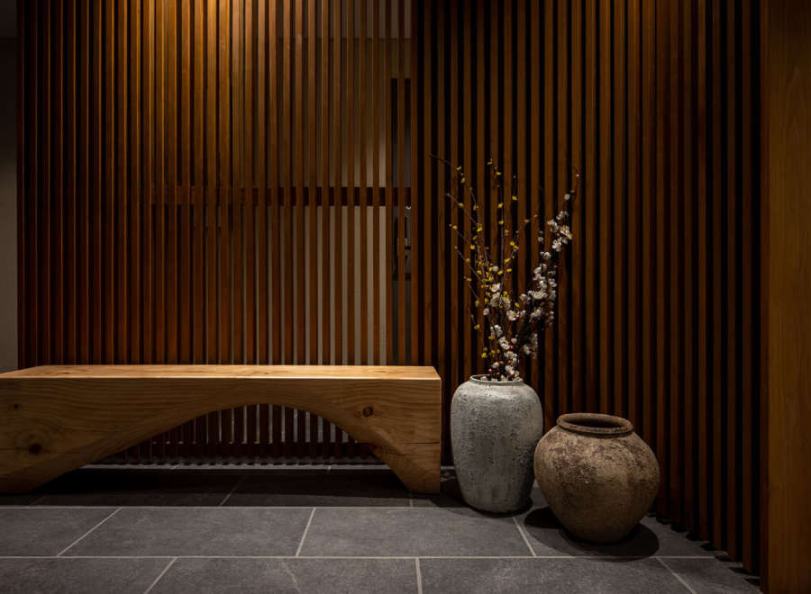 This modern and minimalist hallway features a stunning wooden slat wall, a rustic wooden bench, and two unique ceramic pots with delicate branches.