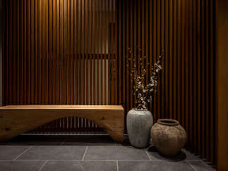 This modern and minimalist hallway features a stunning wooden slat wall, a rustic wooden bench, and two unique ceramic pots with delicate branches.