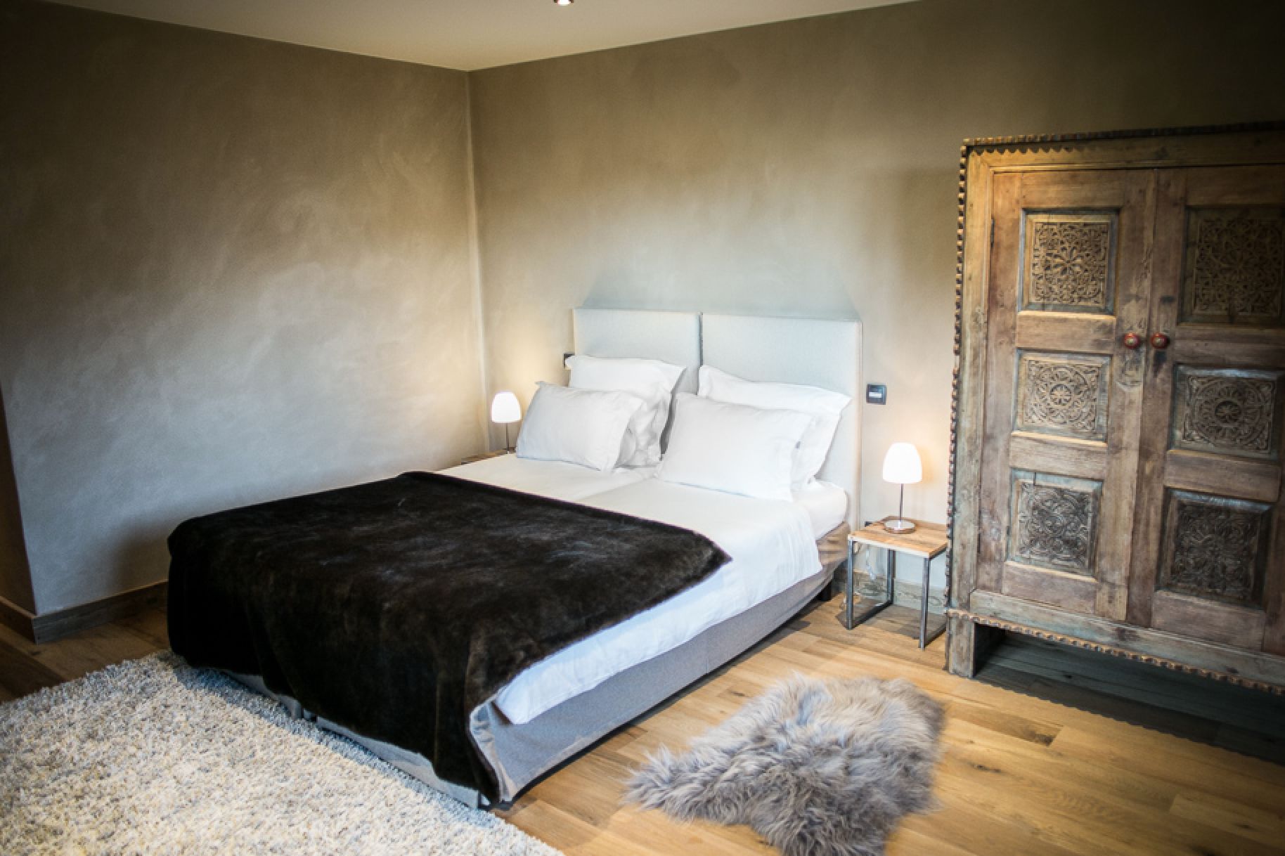 Cozy bedroom with a plush bed, soft rug, and intricately carved wooden wardrobe.