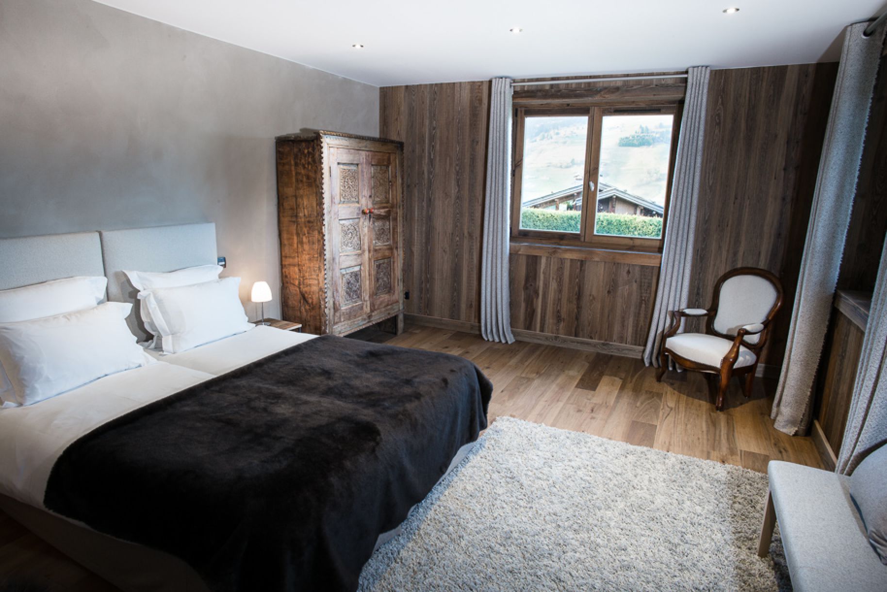 Cozy bedroom with wooden walls and a large window offering scenic views.