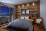This stunning bedroom boasts a cozy atmosphere with a rustic wooden wall, plush bedding, and a comfortable armchair.