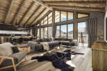 This stunning chalet boasts a spacious open-plan living area with exposed wooden beams, large windows offering breathtaking mountain views, and a cozy fireplace.
