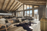 This stunning chalet boasts a spacious open-plan living area with exposed wooden beams, large windows offering breathtaking mountain views, and a cozy fireplace.