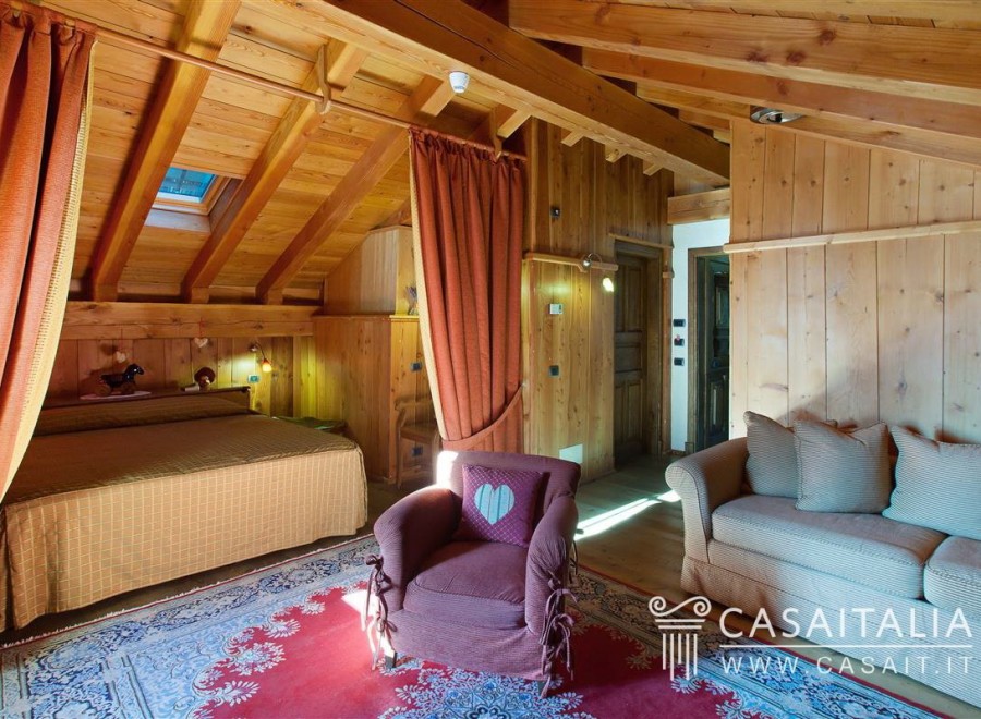 Cozy chalet bedroom with wooden beams, skylight, and ensuite sitting area.