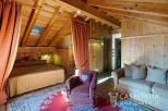Cozy chalet bedroom with wooden beams, skylight, and ensuite sitting area.