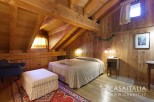 Cozy wooden bedroom with a double bed, ottoman, and armchair.