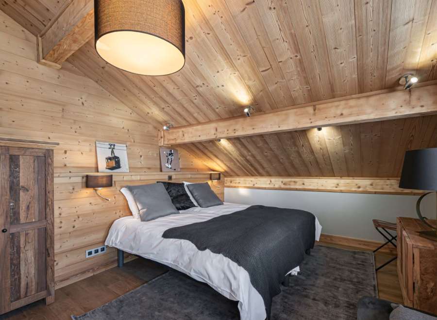 Cozy chalet bedroom with wooden walls and ceiling, featuring a comfortable double bed and rustic wooden furniture.
