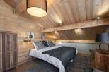 Cozy chalet bedroom with wooden walls and ceiling, featuring a comfortable double bed and rustic wooden furniture.