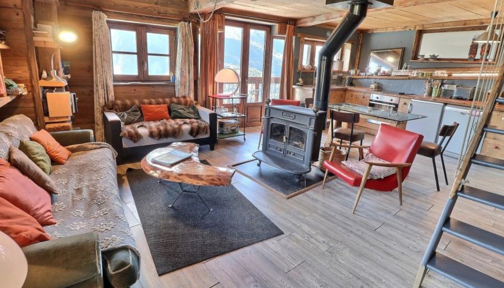 Cozy chalet living room with wood-burning stove, comfy sofas, and large windows offering stunning mountain views.