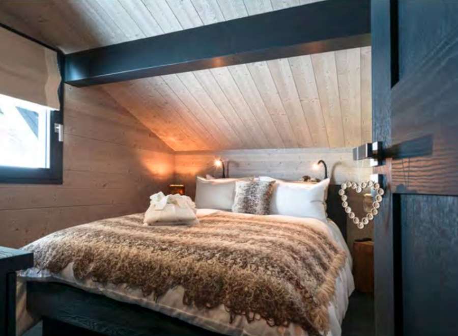 Cozy chalet bedroom with wooden walls and ceiling, featuring a comfortable bed with a thick blanket.