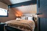 Cozy chalet bedroom with wooden walls and ceiling, featuring a comfortable bed with a thick blanket.